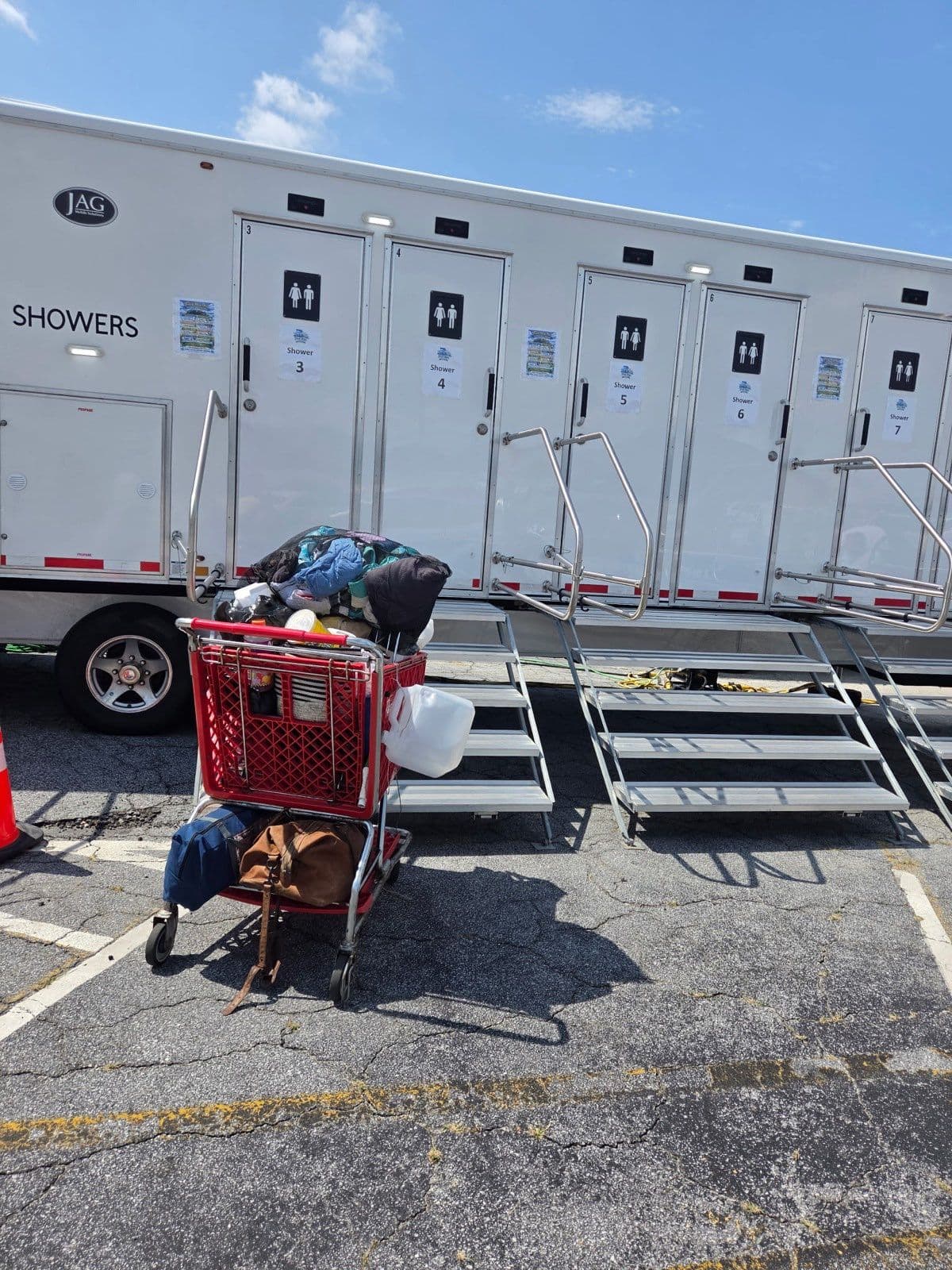 The Fresh Hope shower trailer parked at a service event, with a guest's belongings in a cart beside the steps.
