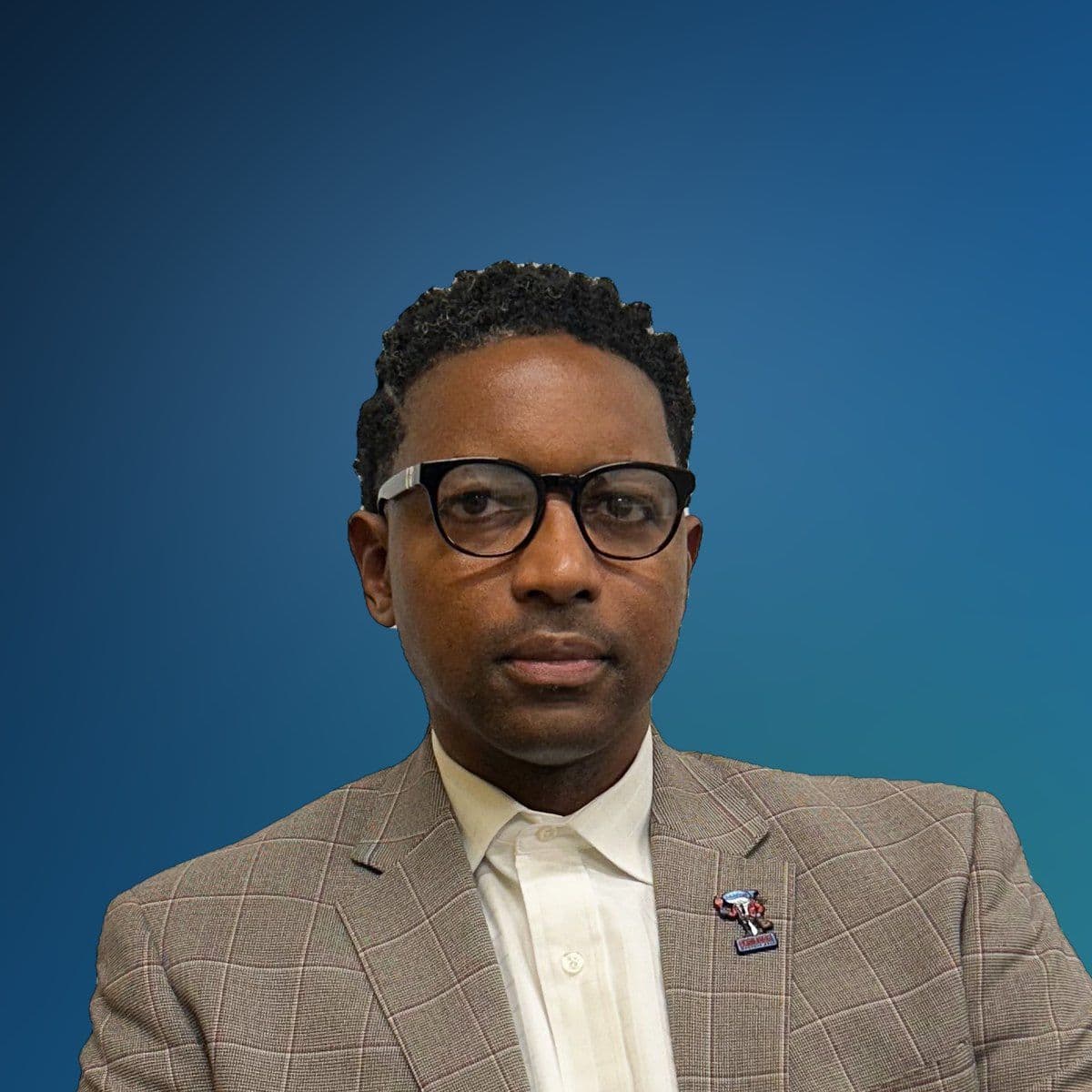Sha’Drach Qawiy in glasses, a cream shirt and a tan checked jacket.